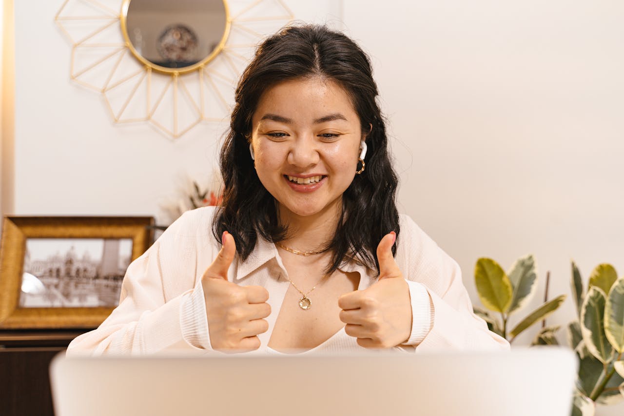 about-us Asian businesswoman giving thumbs up during a successful online meeting, smiling and engaged.